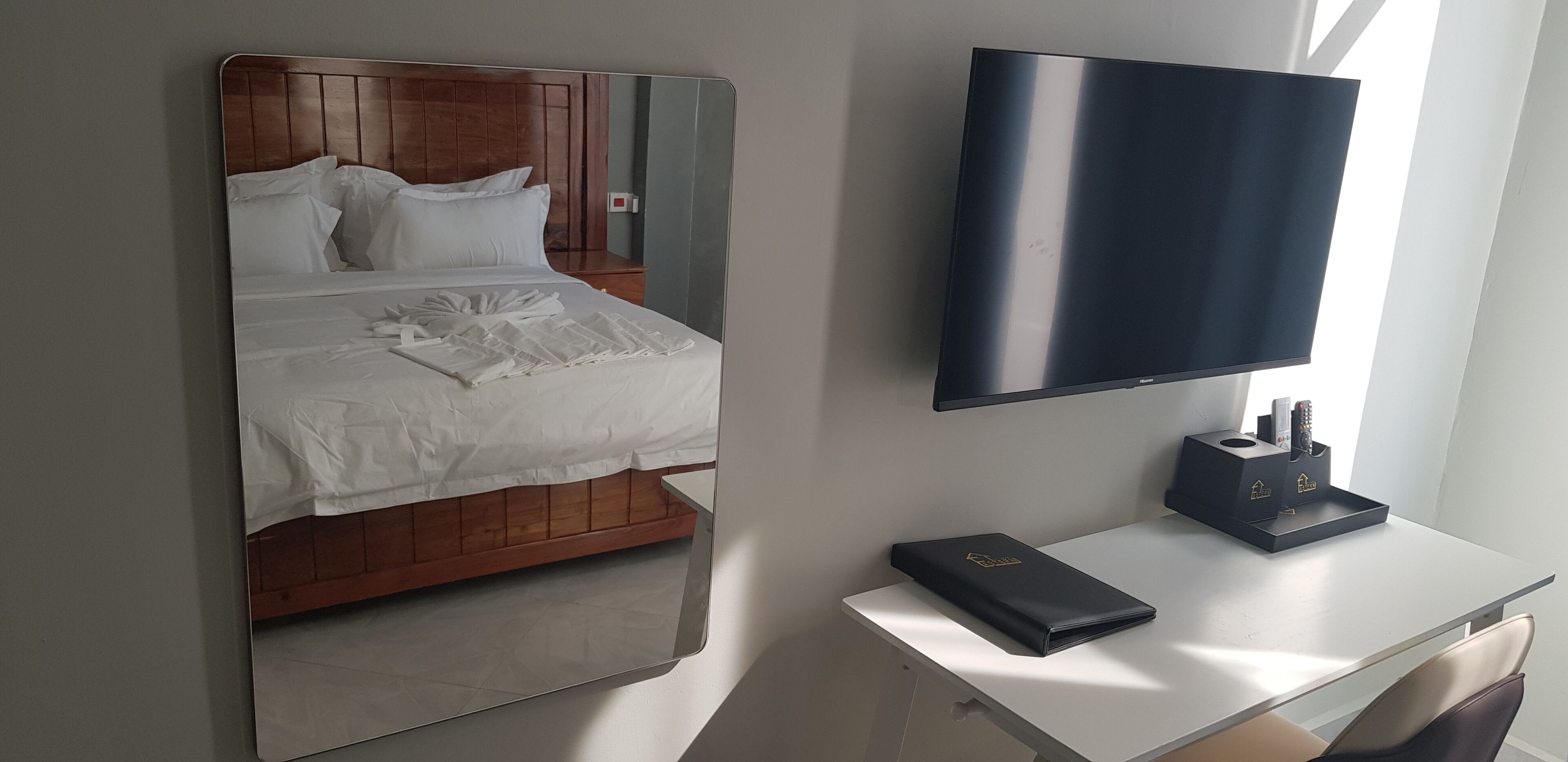 A hotel room with a bed, a TV, a desk, and a mirror.