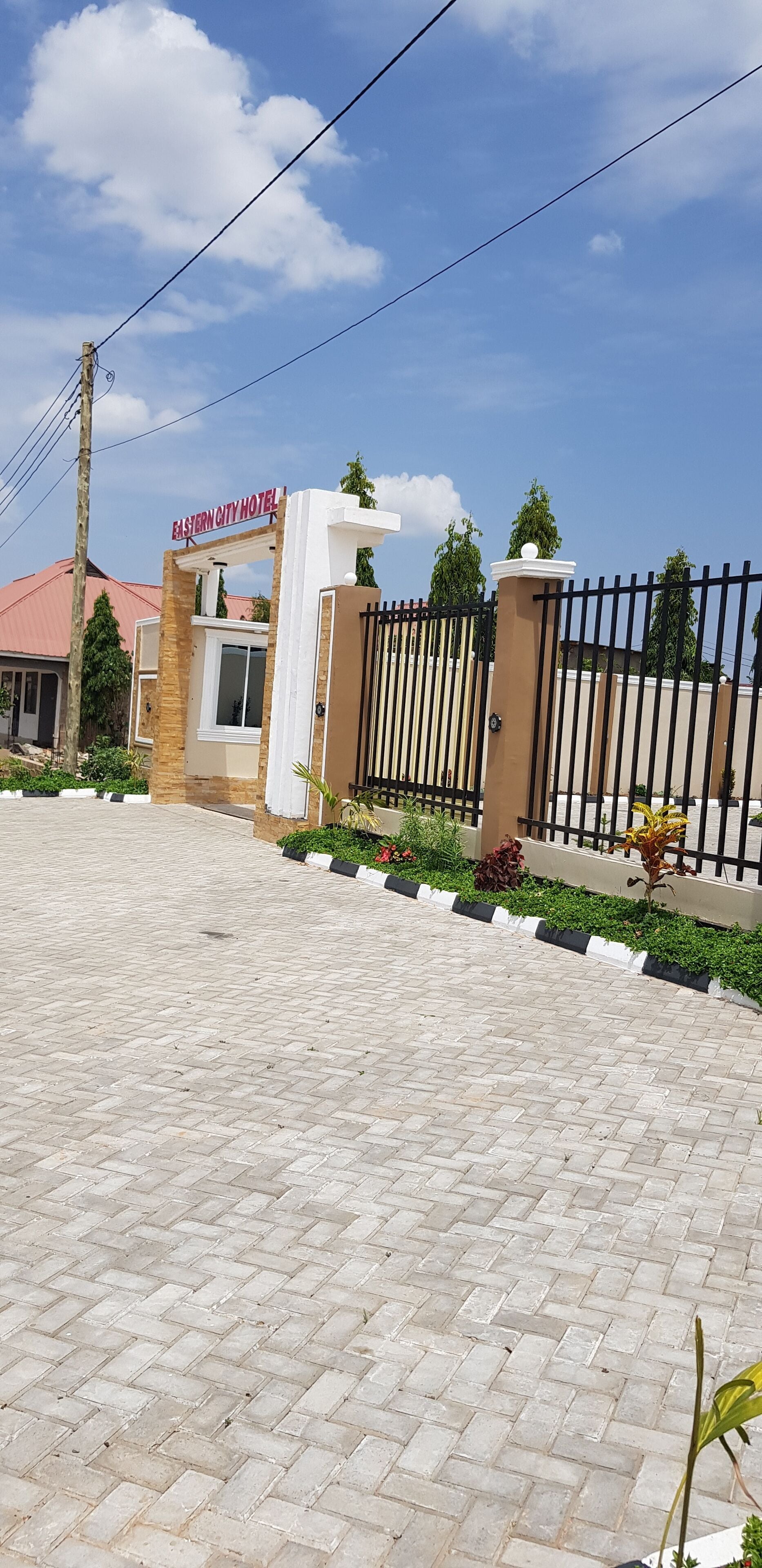 A gated entrance to Eastern City Hotel with a paved driveway and landscaped garden beds.