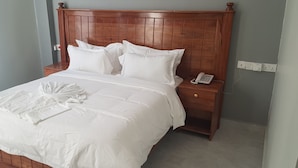 Una cama bien hecha con sábanas y almohadas blancas, un cabecero de madera, una mesita de noche con un teléfono y un enchufe en la pared.