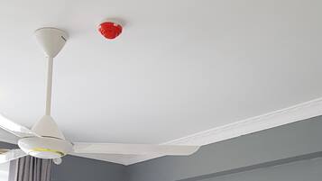 Una habitación de hotel con cama, cabecero de madera, ventilador de techo, equipo de aire acondicionado y ventana con cortinas.