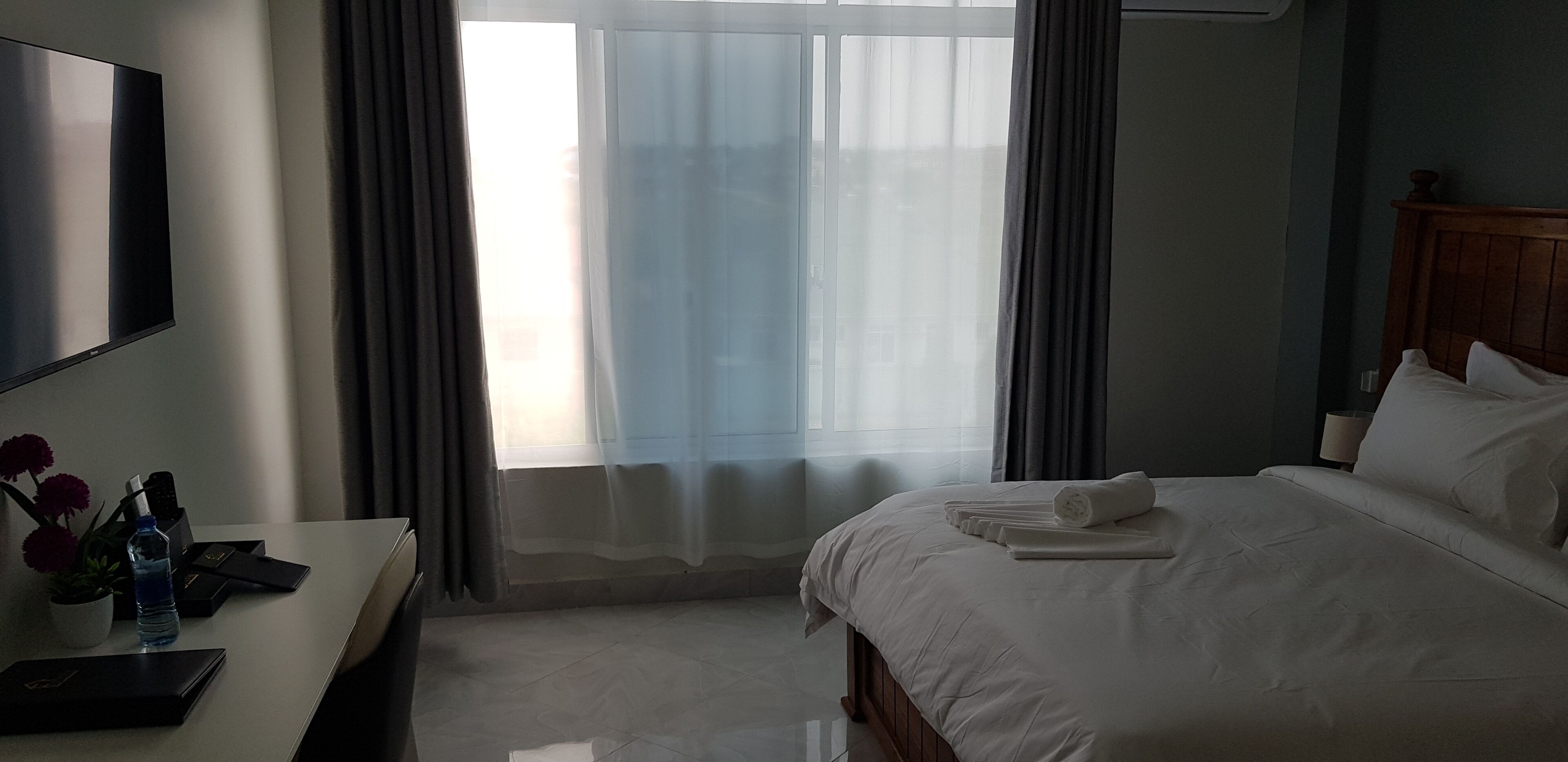Una habitación de hotel con cama, escritorio con laptop, televisor y ventana con cortinas.