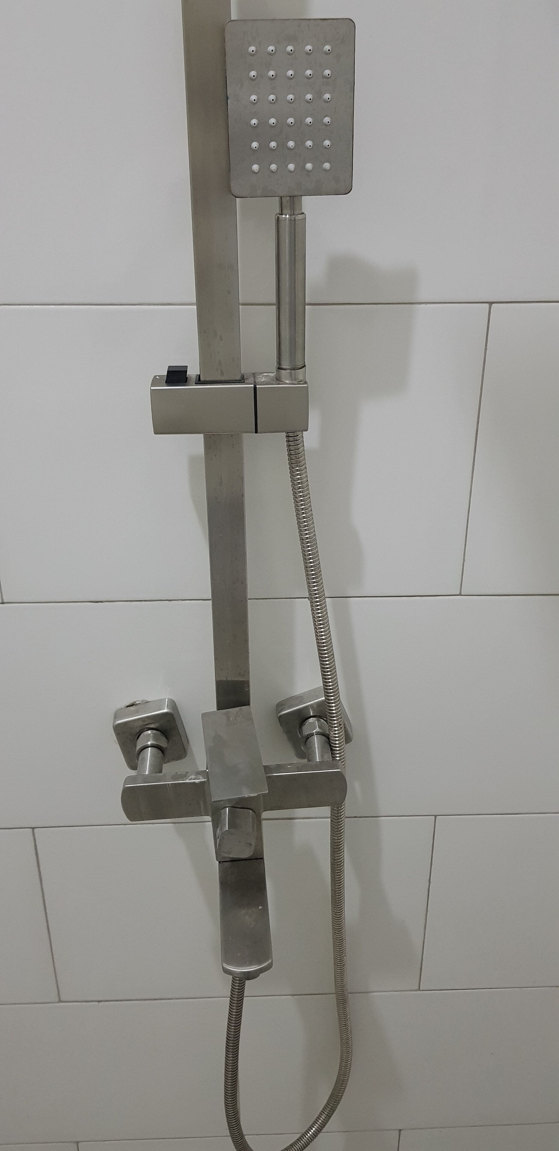 A shower with a handheld showerhead and a fixed wall-mounted showerhead, both mounted on a metal frame.