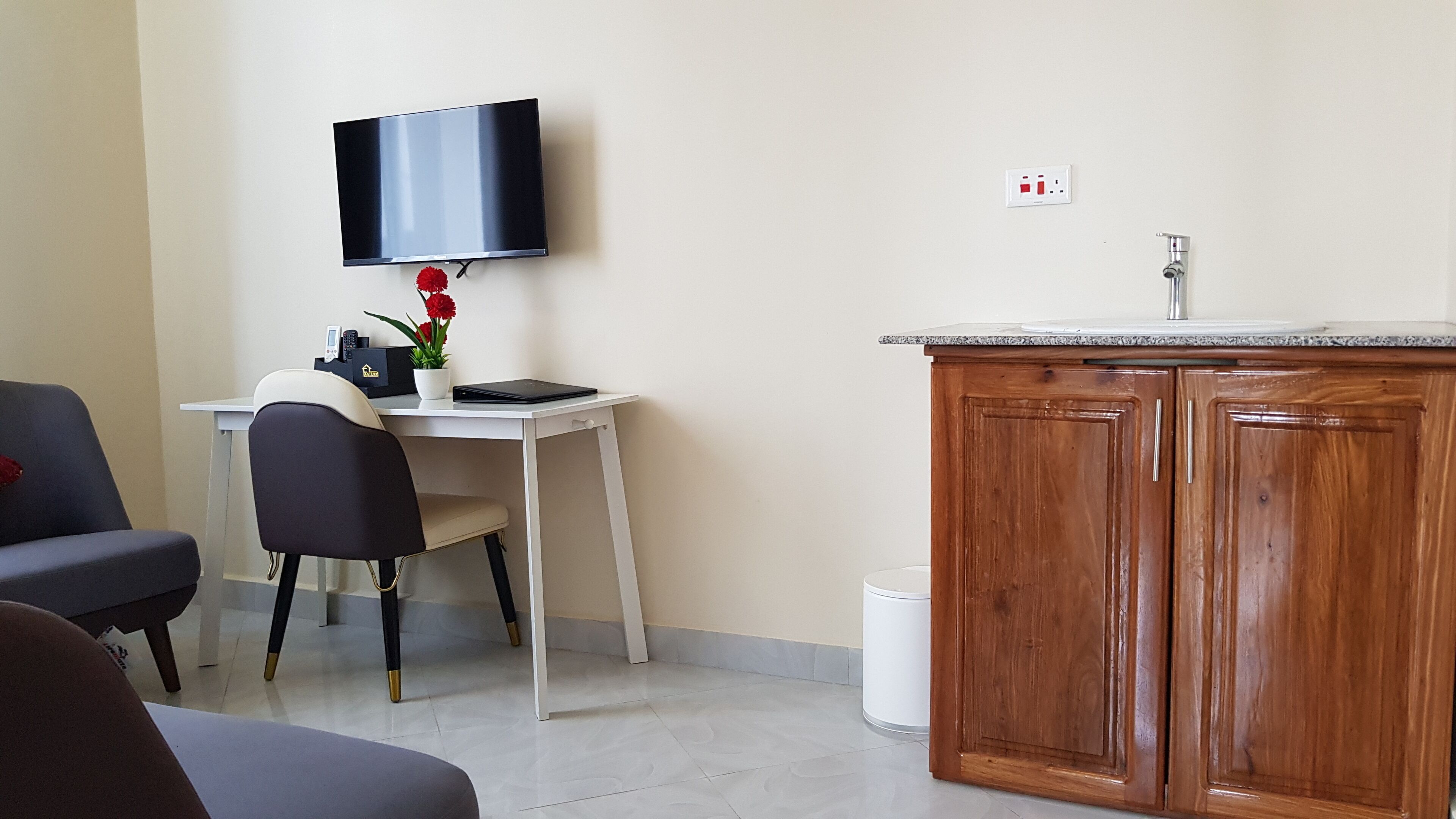 A small, modern room with a desk, chair, television, and wooden cabinets.