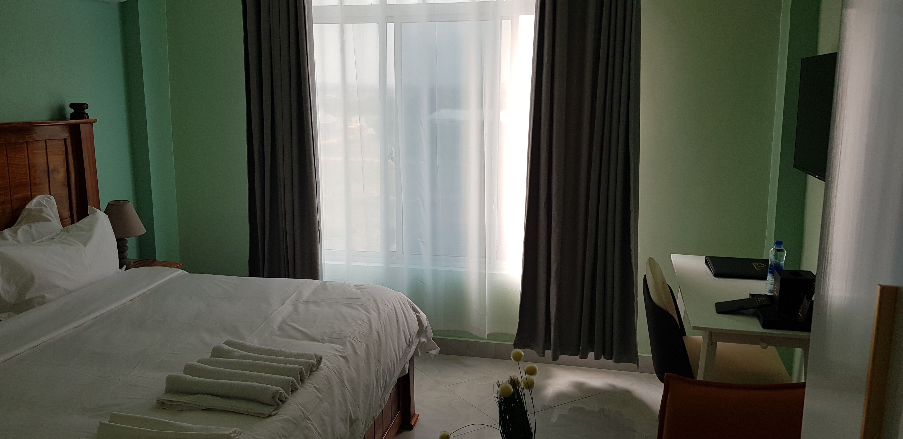 A hotel room with a bed, a desk, a chair, a TV, and a window with curtains.