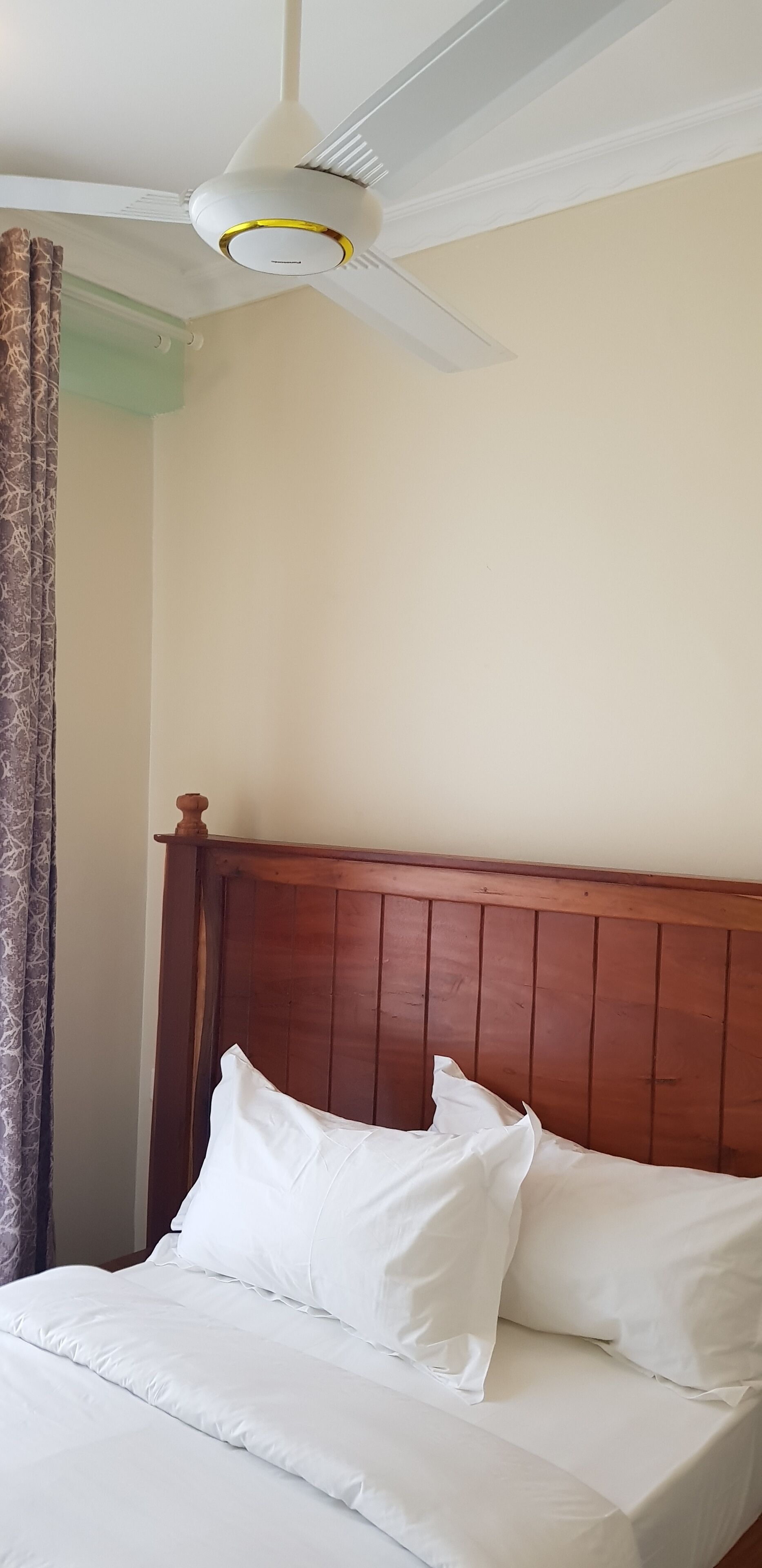 A neatly made bed with white linens and a wooden headboard in a room with a ceiling fan.