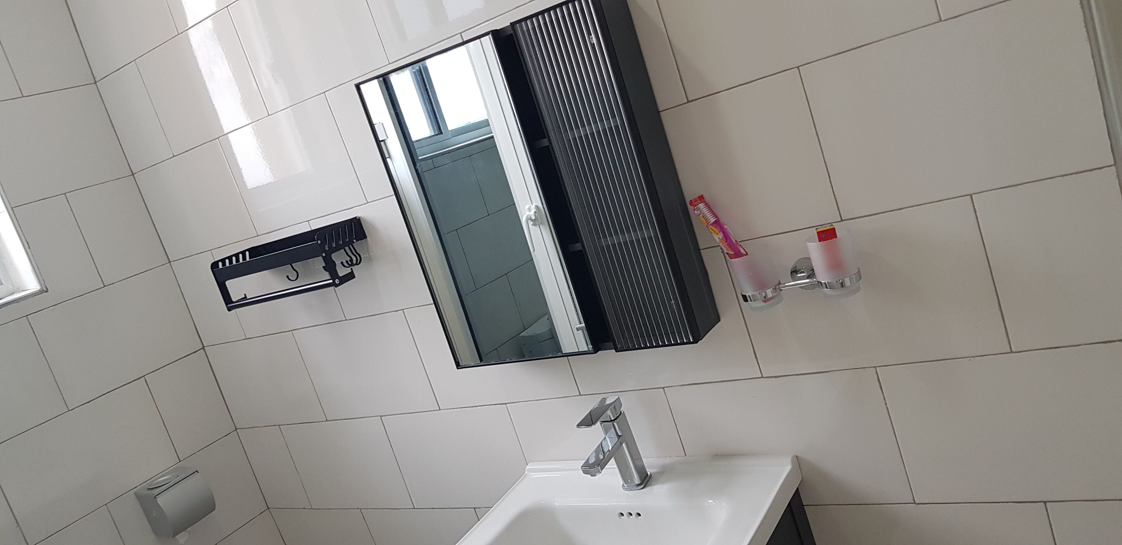 A bathroom with white tiles, a mirror, a sink, and a hand dryer.