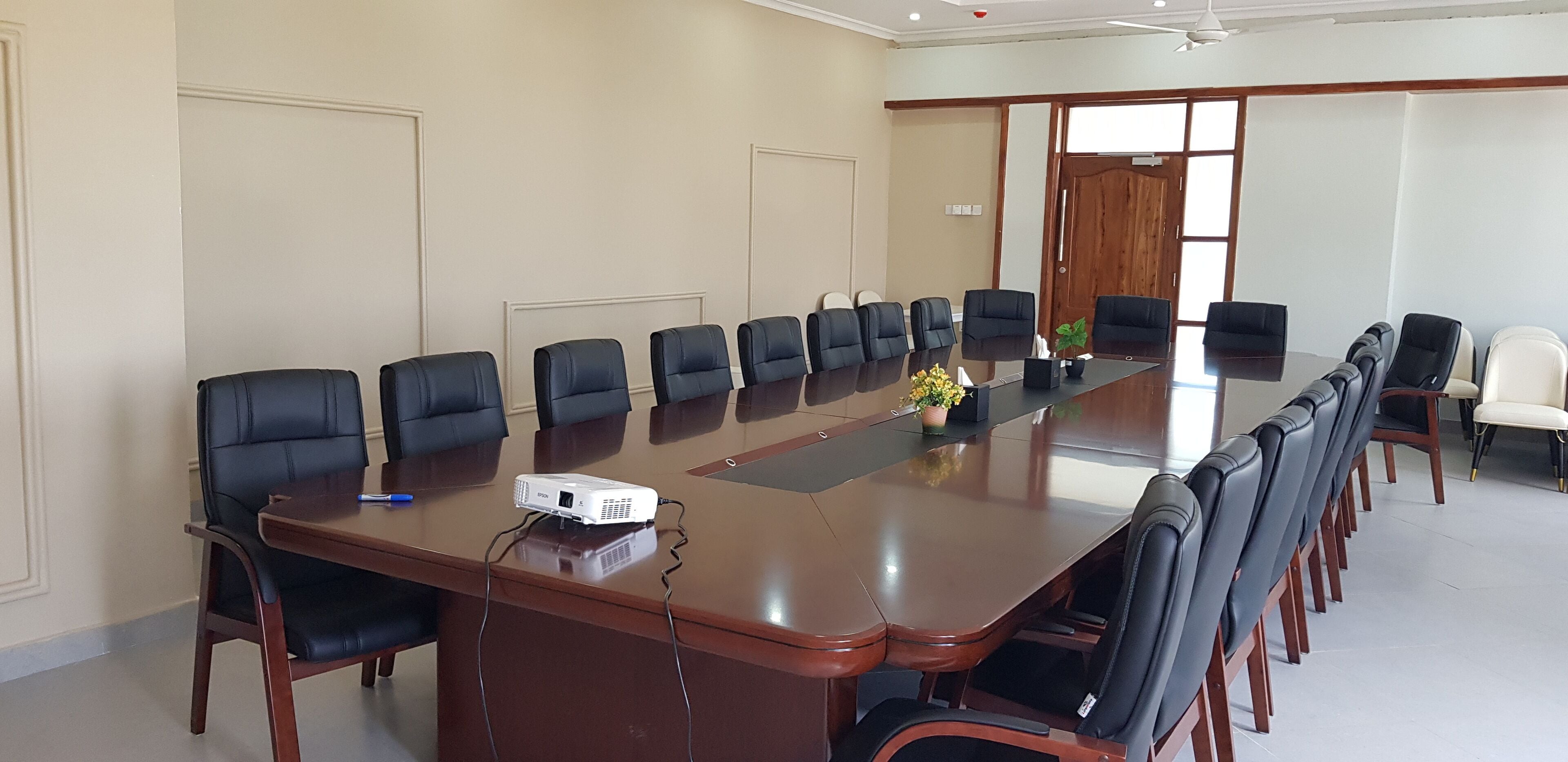 A conference room with a long table, black chairs, a projector, and a potted plant.