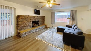 A living room with a stone fireplace, a ceiling fan, a TV mounted on the wall, and a large window with curtains. - Home in Union City
 (Union City)