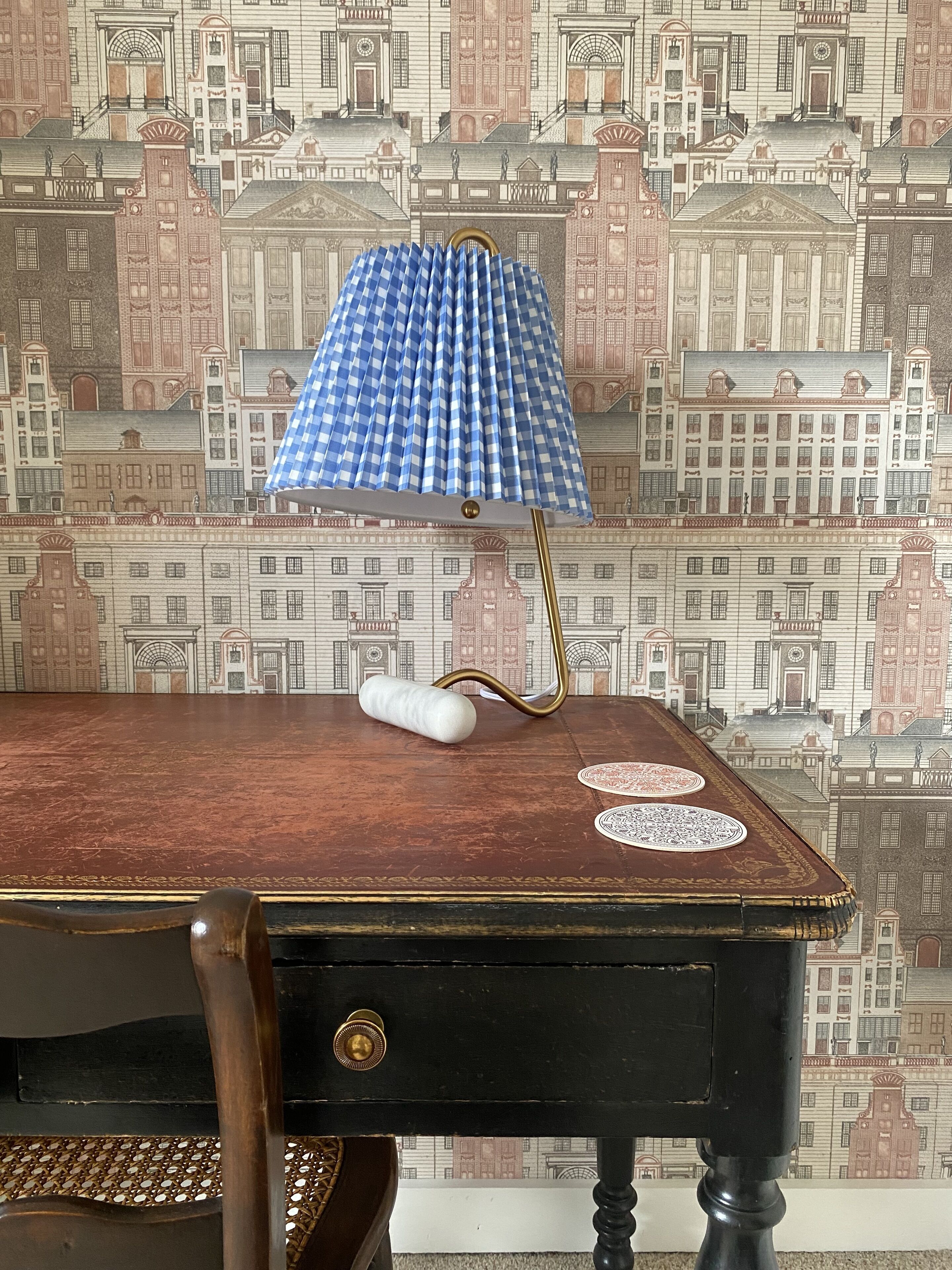 Ein alter Schreibtisch mit einer karierten Lampe, einem weißen zylindrischen Gegenstand und zwei runden Untersetzern.