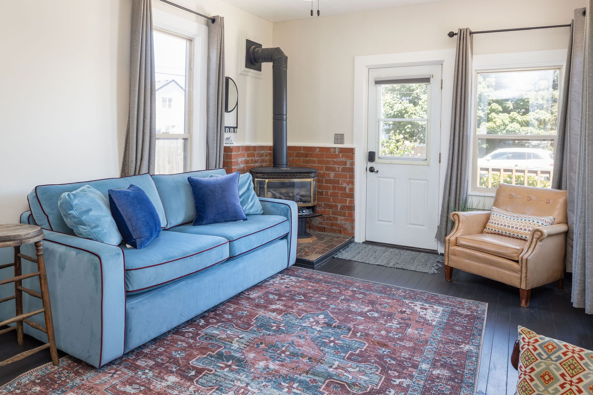 Una sala de estar acogedora con un sofá azul, un tapete estampado, un sillón de cuero y una estufa de leña.