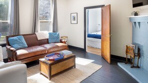 Un salón acogedor con un sofá de cuero marrón, una mesa de centro de madera y una cama azul al fondo.