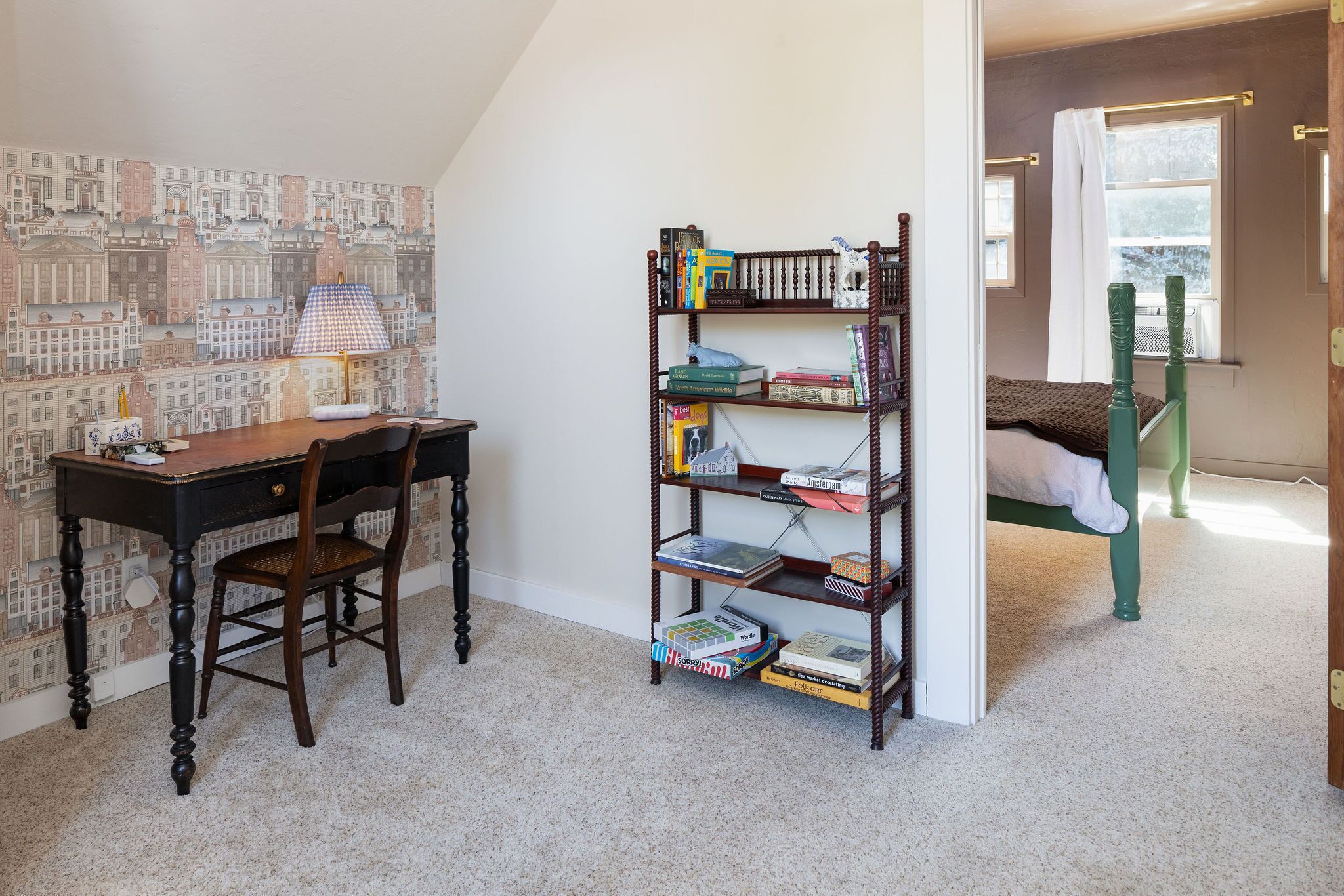 A room with a desk, chair, bookshelf, and a bed with a green headboard.