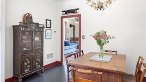 Un comedor con una mesa de madera, sillas, un aparador con motivos florales y un jarrón con flores.