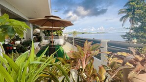 A balcony with outdoor seating, potted plants, and a view of the sea.