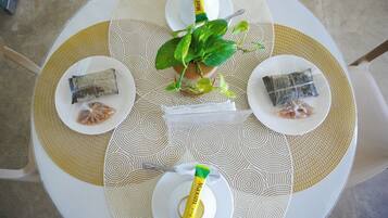A round table with a white and beige patterned tablecloth, two plates with wrapped food items, a green plant in a pot, and a yellow tube on the table.