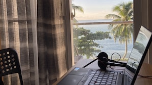 A laptop on a desk with a view of the ocean and palm trees through a window. - Happy Island Inn (Virac)