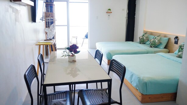 A room with a dining table, two beds, a fan, and a window.
