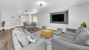 A modern living room with a grey sofa, a wooden coffee table, and a TV mounted on the wall.