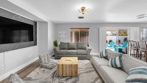 A modern living room with a grey sofa, a wooden coffee table, and a TV mounted on the wall.