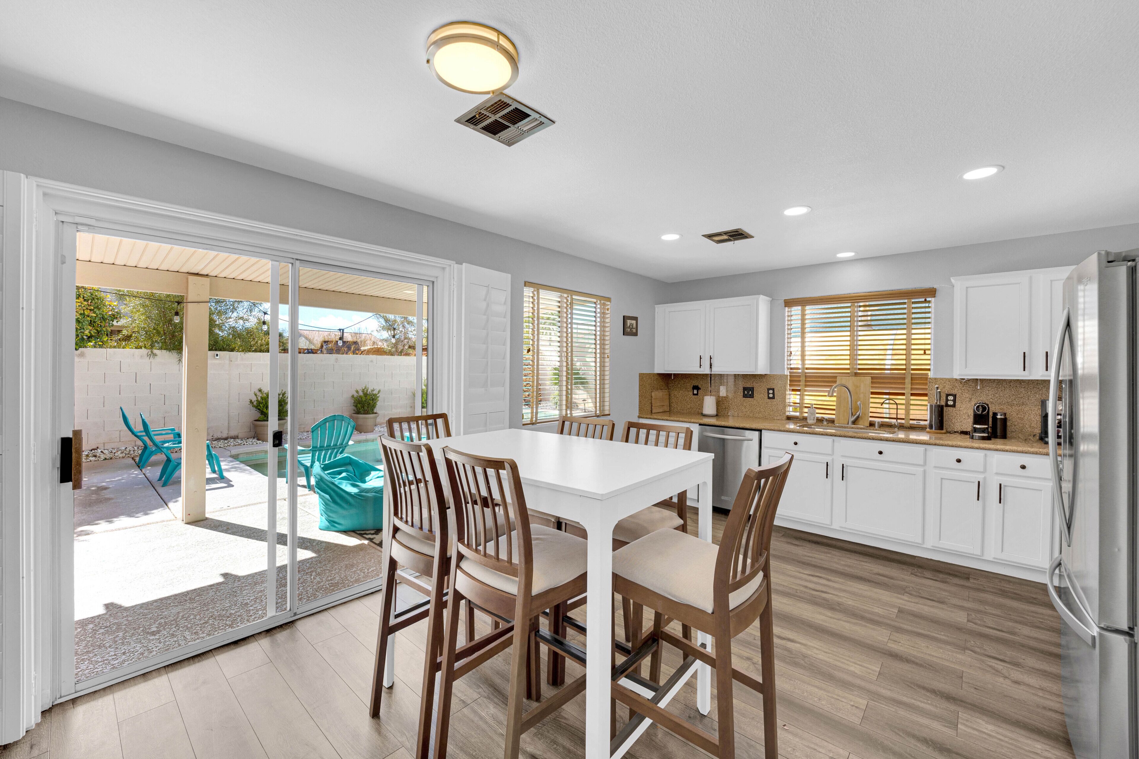 Una cocina moderna con armarios blancos, un refrigerador de acero inoxidable y un comedor con una mesa blanca y sillas de madera.