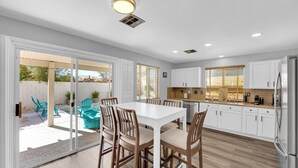 A modern kitchen with white cabinets, a stainless steel refrigerator, and a dining area with a white table and wooden chairs.