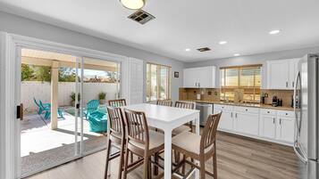 Una cocina moderna con armarios blancos, un refrigerador de acero inoxidable y un comedor con una mesa blanca y sillas de madera.