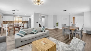 A spacious living area with a grey sofa, wooden coffee table, and a dining table with chairs.