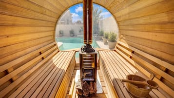 Una sauna con interior de madera, un calentador central y vista a una piscina exterior.