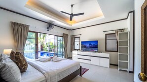 Een moderne hotelkamer met een groot bed, een plafondventilator, een televisie en uitzicht op een zwembad.
