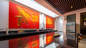 Een moderne hotellobby met een glanzende zwarte marmeren vloer, grote rode en gele kunstwerken aan de muren en een zithoek met een ventilator en een koelkast.
