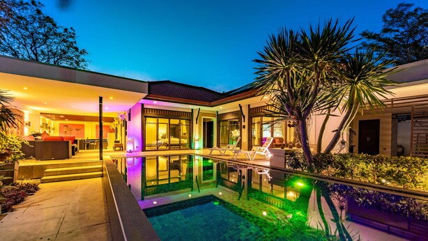 Een modern huis met een zwembad, een overdekt terras en een goed verlicht interieur.