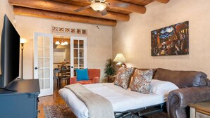 Une chambre à coucher avec un lit, une télévision, un ventilateur de plafond, un tableau et un plafond en bois.