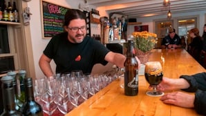 Un bar, avec un barman en train de verser une boisson dans un verre, entouré de verres et de bouteilles de vin vides.