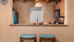 Une cuisine avec un plafond en bois, une horloge au mur et deux tabourets de bar.