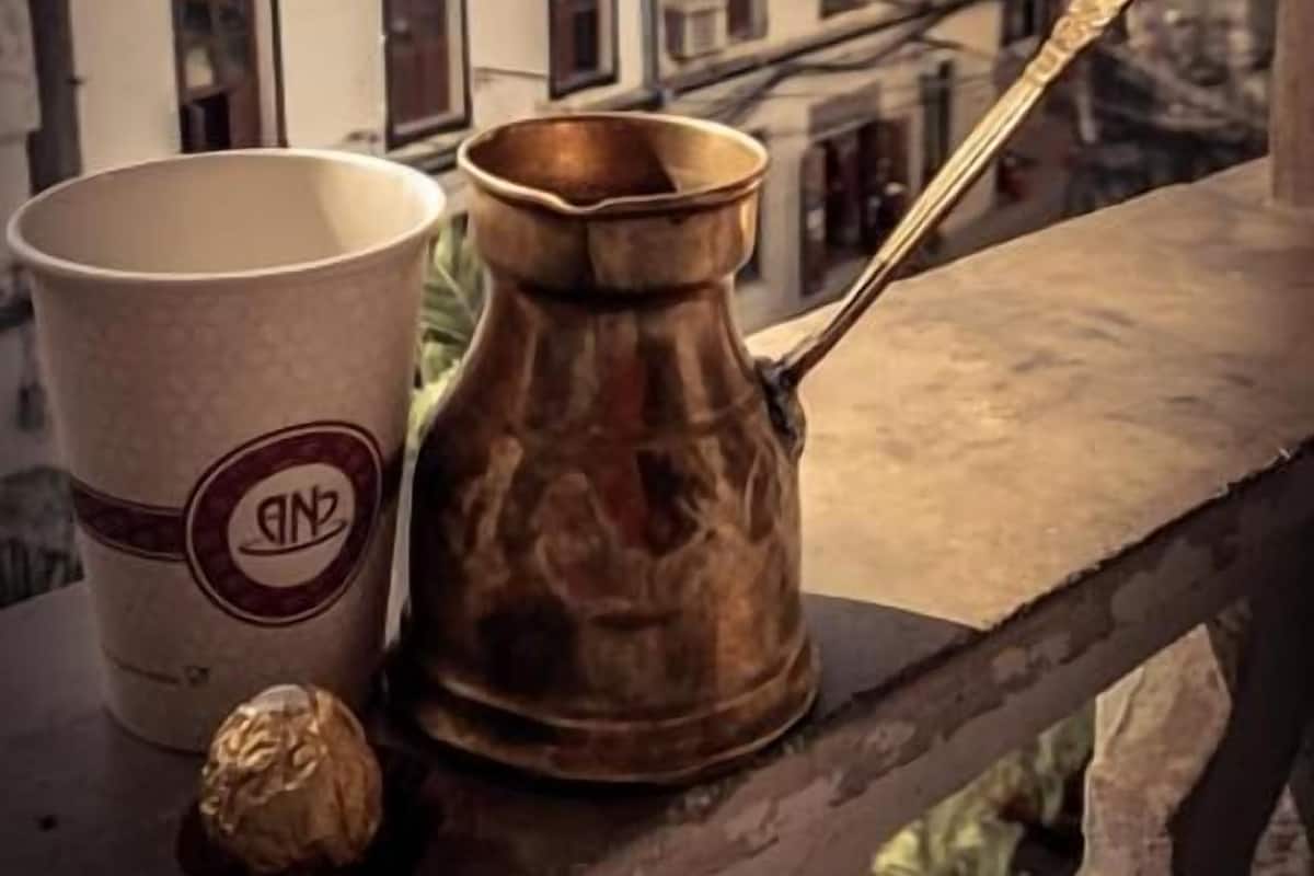 Une tasse à café et une cafetière en laiton sur un balcon donnant sur des immeubles.