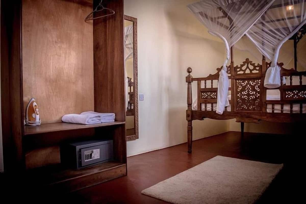Un lit en bois avec un baldaquin, un miroir, une étagère avec des serviettes pliées et un petit coffre-fort.