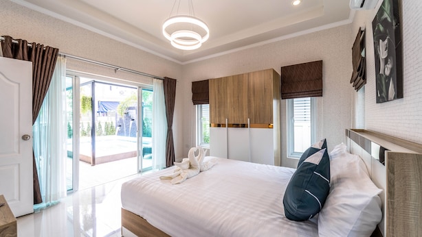 A modern hotel room with a large bed, a wooden headboard, a ceiling light, and a view of the outside. - New 2 Bedroom Pool Villa C882 (Hua Hin)