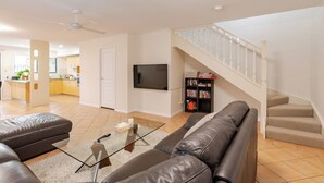 A modern living room with a sofa, a coffee table, a TV, and a staircase leading to an upper floor. - Happy haven at Eight Mile (Eight Mile Plains)
