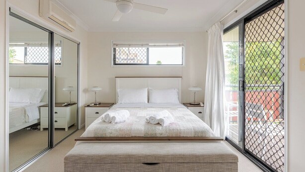 A bedroom with a bed, bedside tables, a ceiling fan, and a large window. - Happy haven at Eight Mile (Eight Mile Plains)