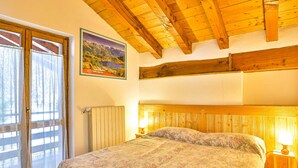 A bedroom with a wooden ceiling, a bed with floral bedding, two bedside lamps, and a window with curtains. - Apartment La Gran Becca - ID 530 (Antey-Saint-Andre)