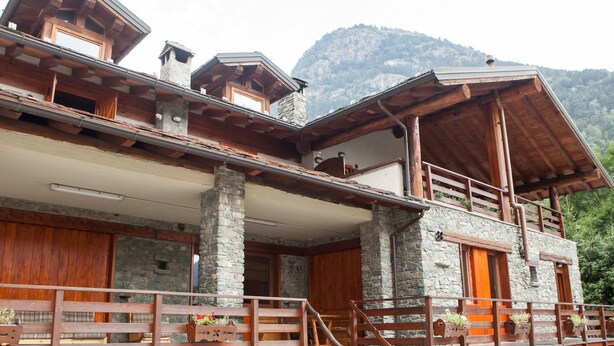 A rustic mountain lodge with a stone facade, wooden balconies, and a staircase leading to the upper level. - Apartment La Gran Becca - ID 530 (Antey-Saint-Andre)