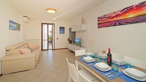 A dining area with a table set for four, a sofa, and a view of the outdoors. - Appartamento Chiaretto (Moniga del Garda)