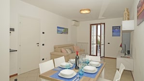 A dining area with a table set for four, a sofa, and a TV on a stand. - Appartamento Chiaretto (Moniga del Garda)