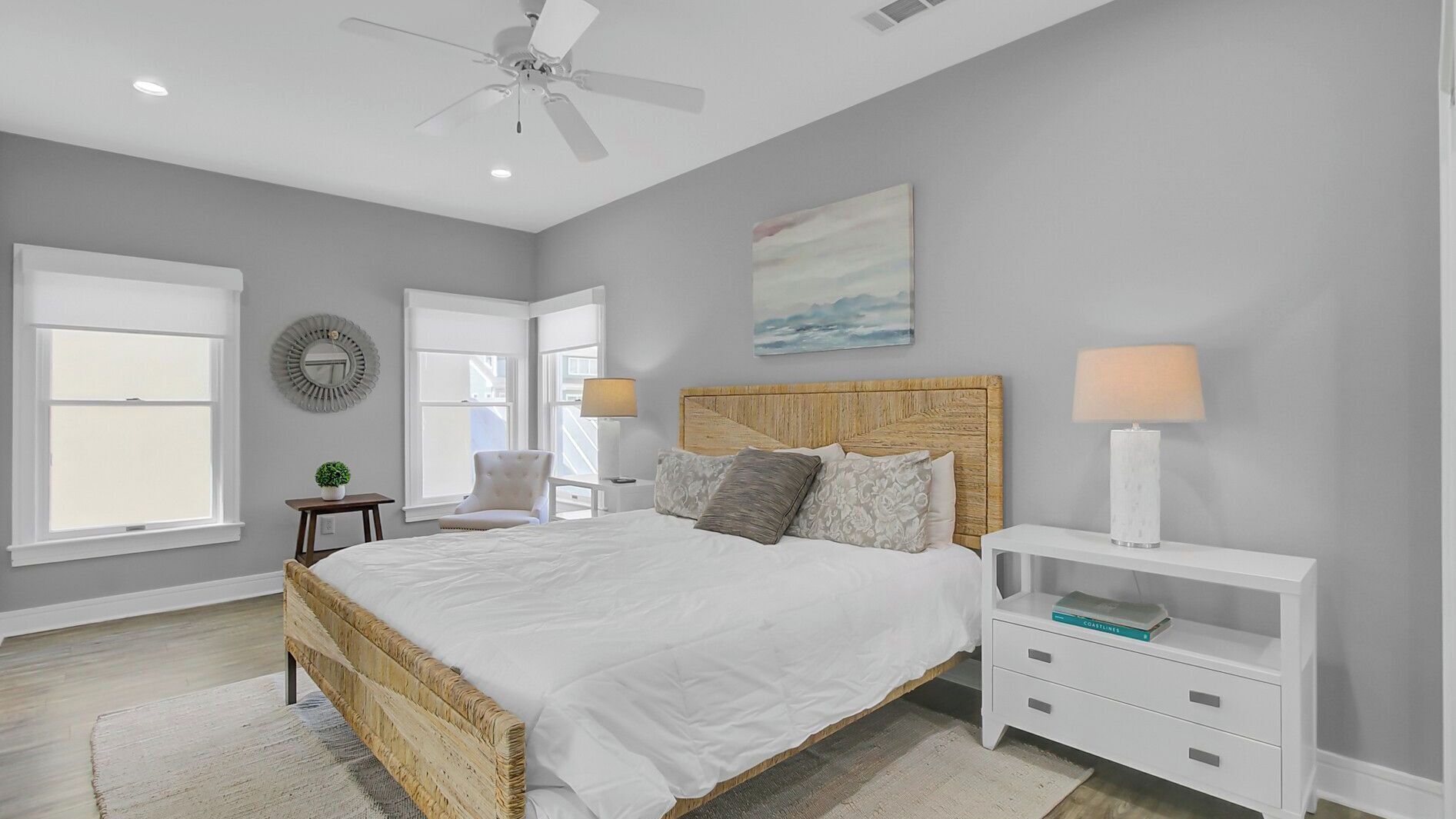 A bedroom with a bed, bedside tables, a ceiling fan, and a painting on the wall.