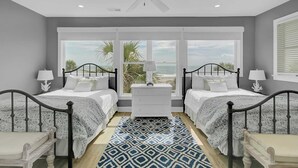 A bedroom with two beds, a ceiling fan, a nightstand, a window with a view of the beach, and a patterned rug. - 109 Grand Pavilion by Avantstay Beachfront Views (Isle of Palms)