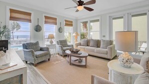 A spacious living room with a ceiling fan, large windows with blinds, a sofa, armchairs, a coffee table, and a lamp. - 109 Grand Pavilion by Avantstay Beachfront Views (Isle of Palms)