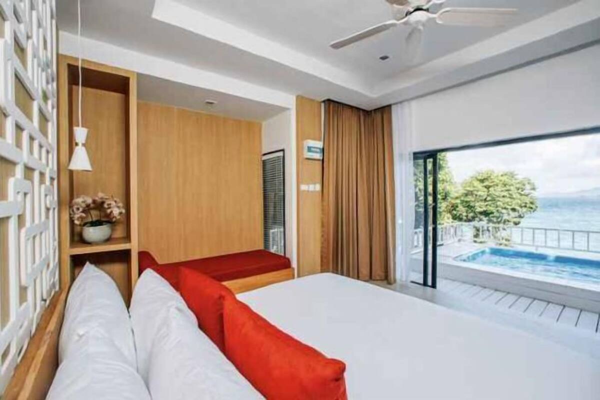 A modern hotel room with a large bed, a view of the sea, and a balcony with a pool.