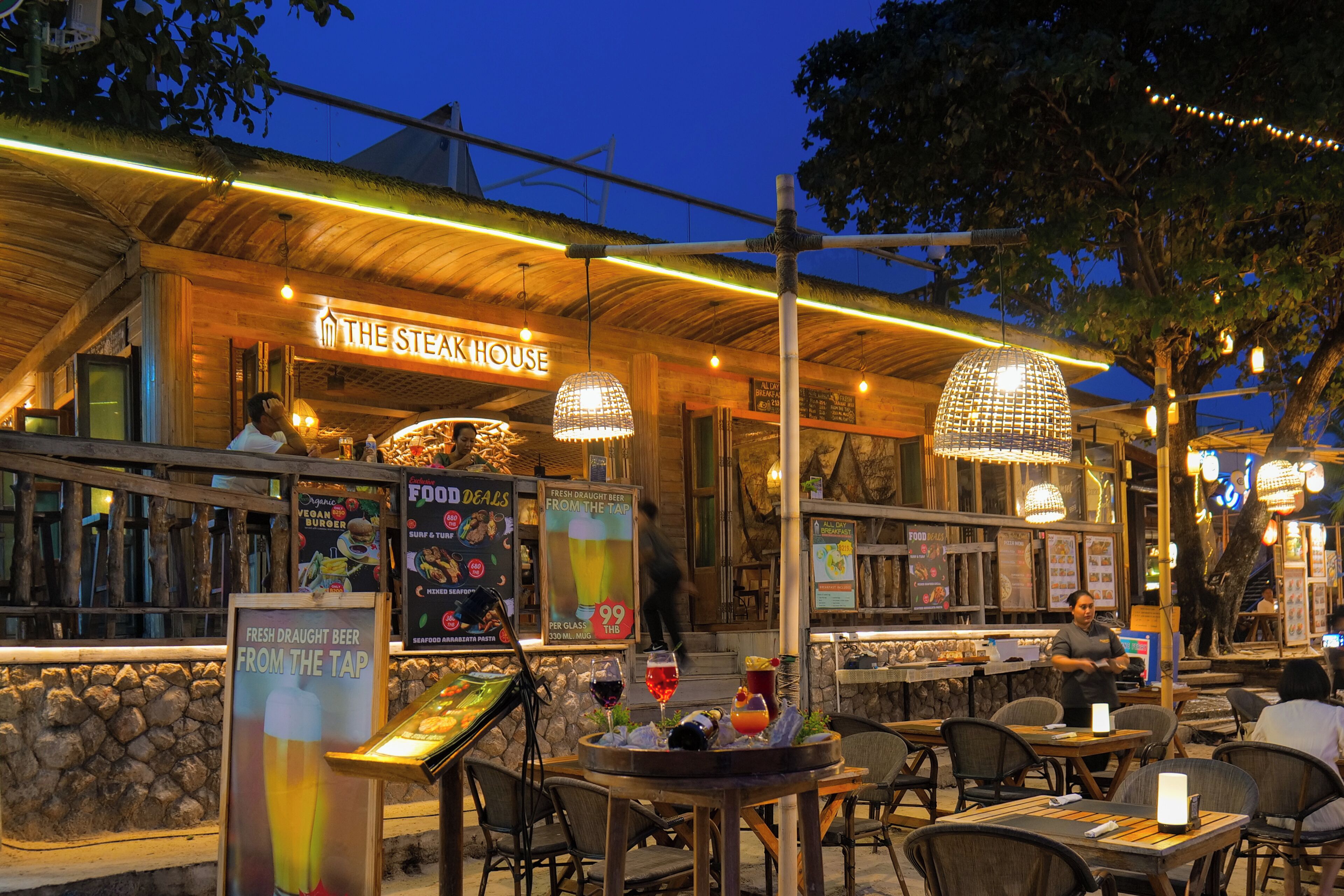 An outdoor dining area at The Steak House with tables, chairs, and hanging lights.