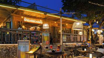 An outdoor dining area at The Steak House with tables, chairs, and hanging lights.