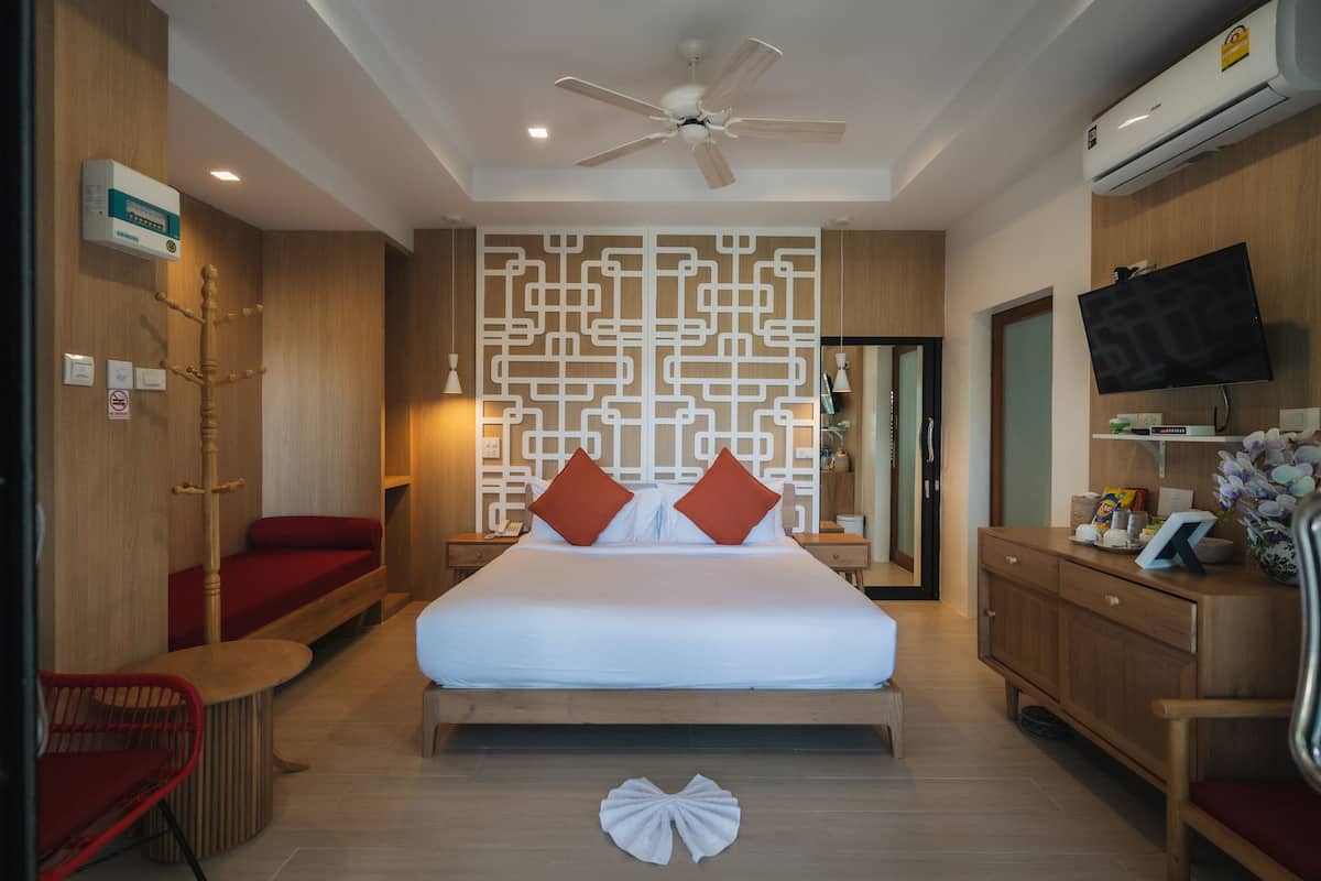 A hotel room with a large bed, a ceiling fan, a TV, a wooden wardrobe, and a wall-mounted air conditioner.